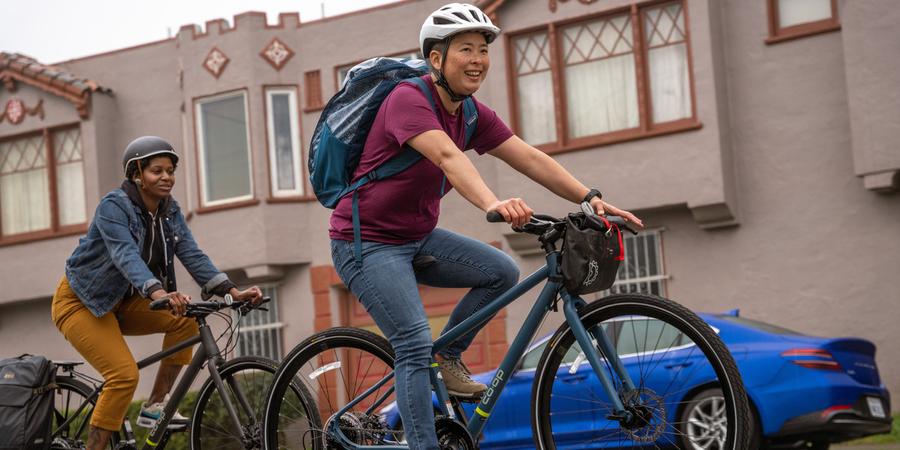 Two people riding bikes along in an urban neighborhood