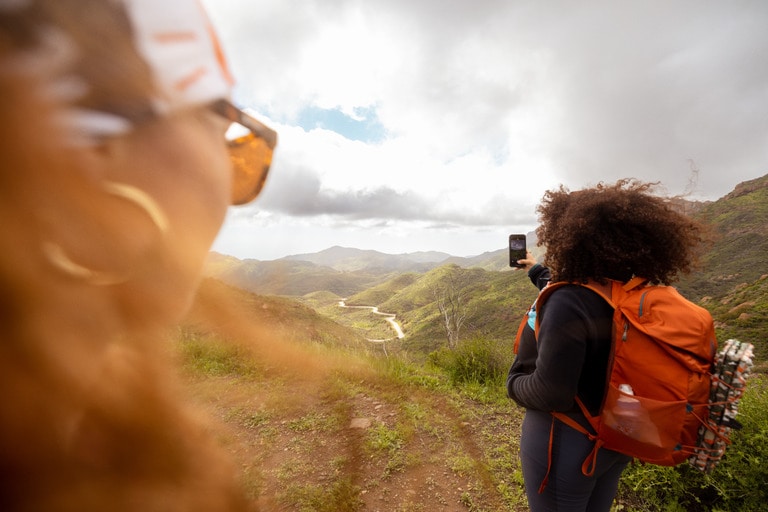 A person wearing a full daypack takes a selfie on a ridge