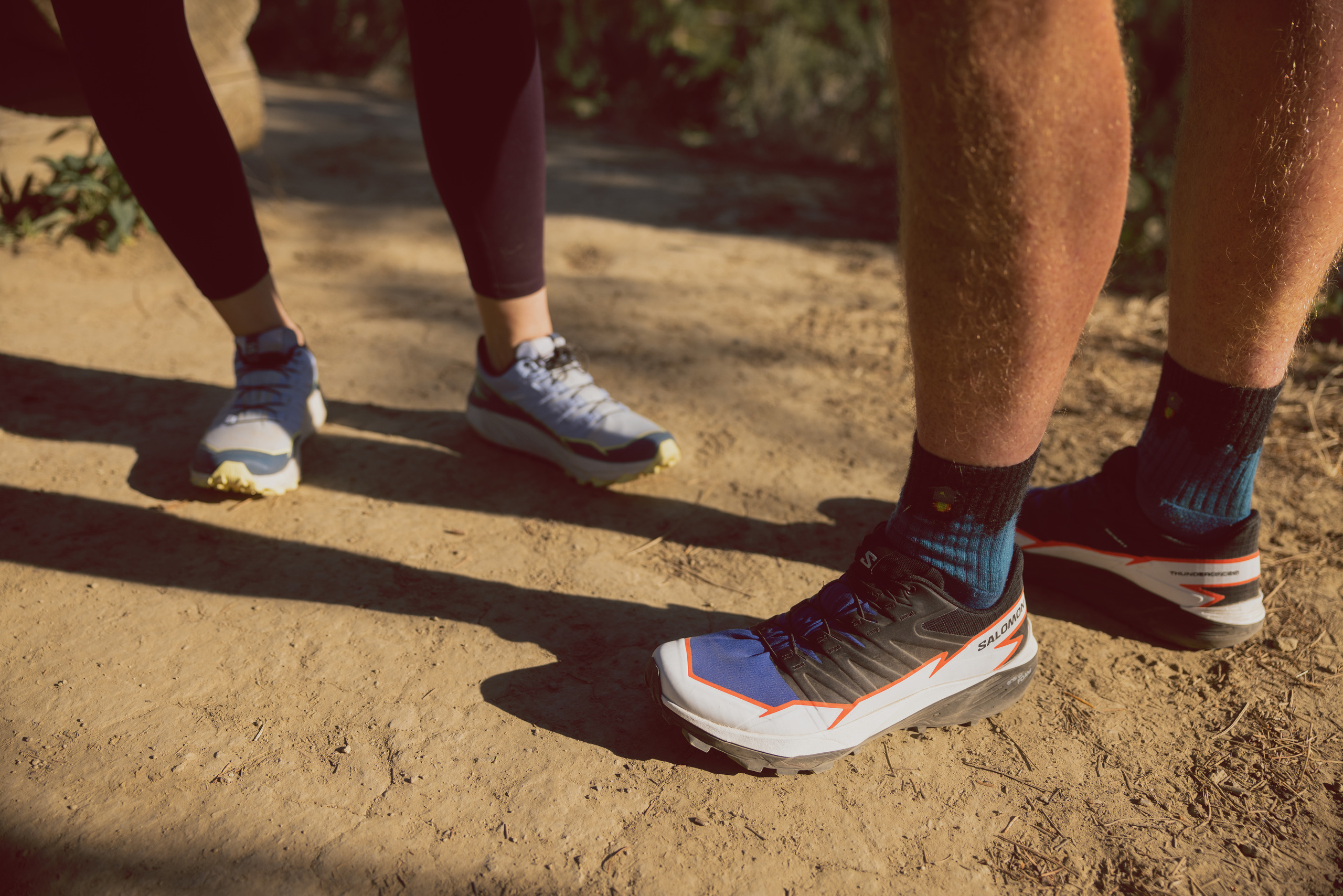 A from-the-leg-down image of a man and a woman each sporting the Salomon Thundercross trail-running shoes