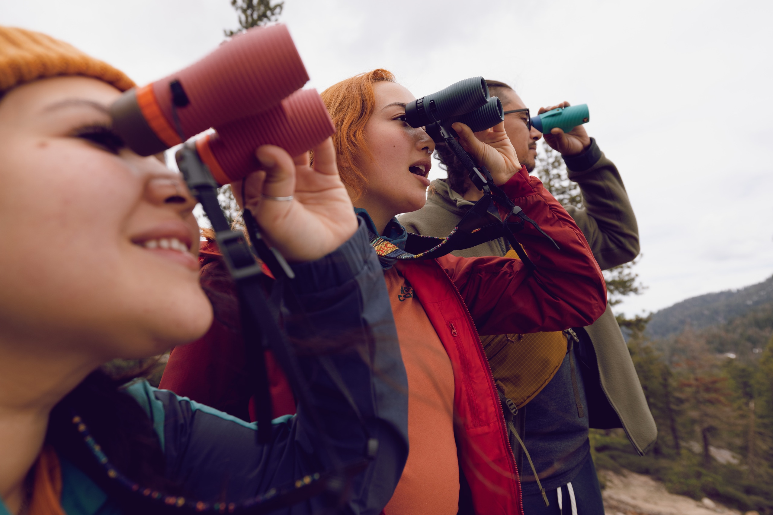 Three people looking through their Nocs Provisions binoculars, with the Nocs Provisions Woven Tapestry Strap
