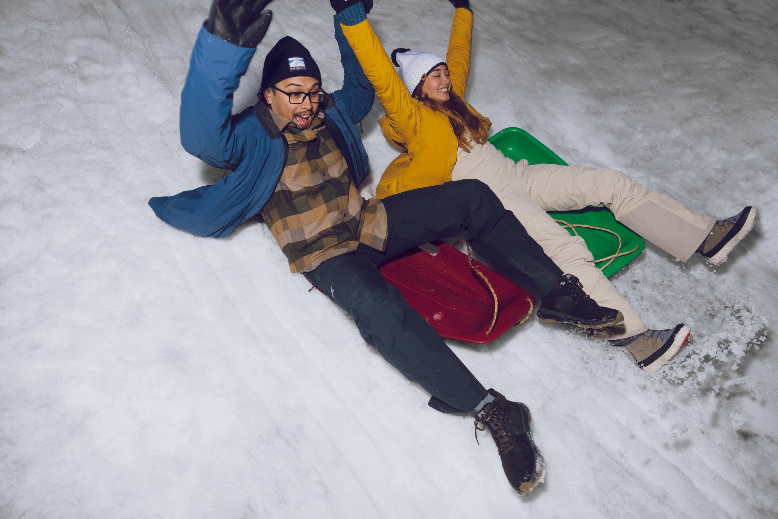 Two people sled down a snowy hill next to each other.