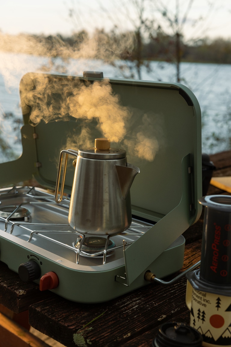 A kettle steaming on a stove next to an AeroPress coffee maker