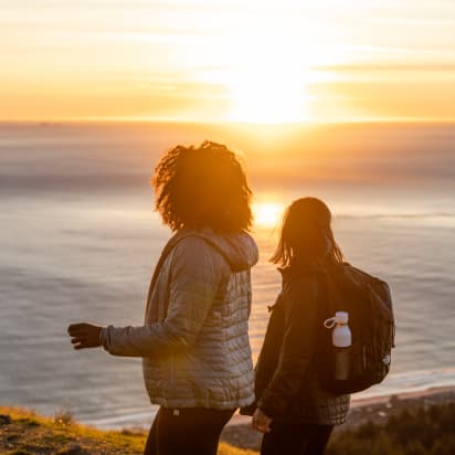 two hikers watch the sun set over the ocean