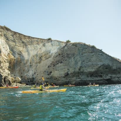 a group of kayaks paddle near a seaside cliff