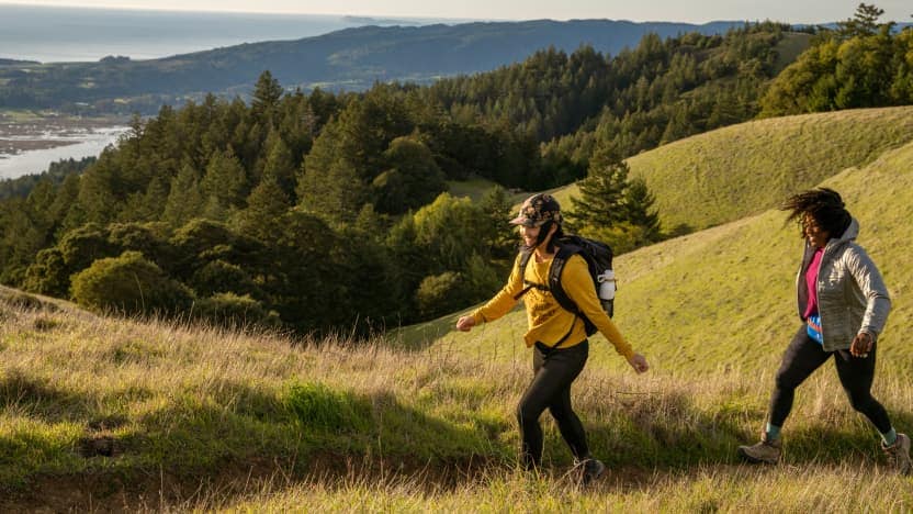 Two women hike a grassy trail.