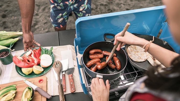 A camper makes sausages on a two-burner stove.