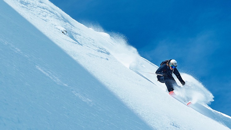A downhill skier on a steep slope with blue sky in the background