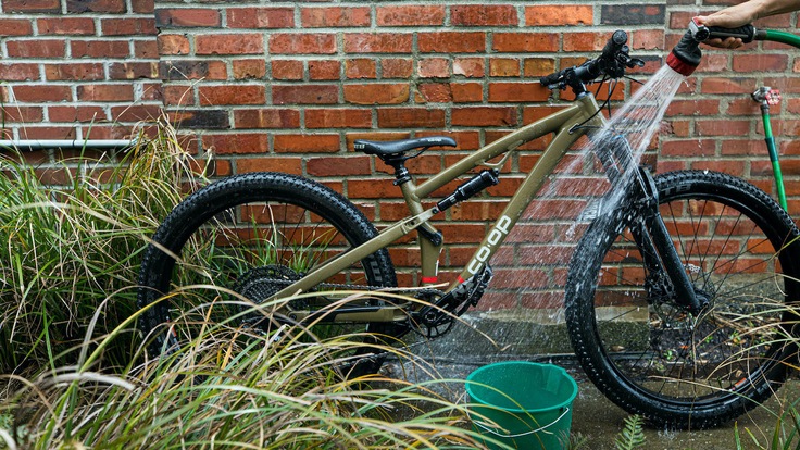 Hosing off a dirty bike that's leaned up against a brick wall