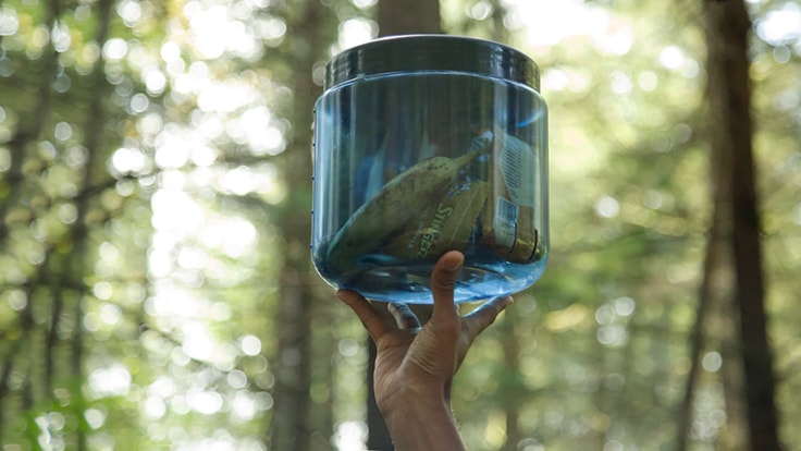 A person's hand holding a bear canister with food in it