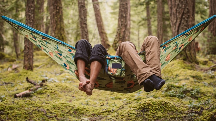Two people sit in a hammock in the woods