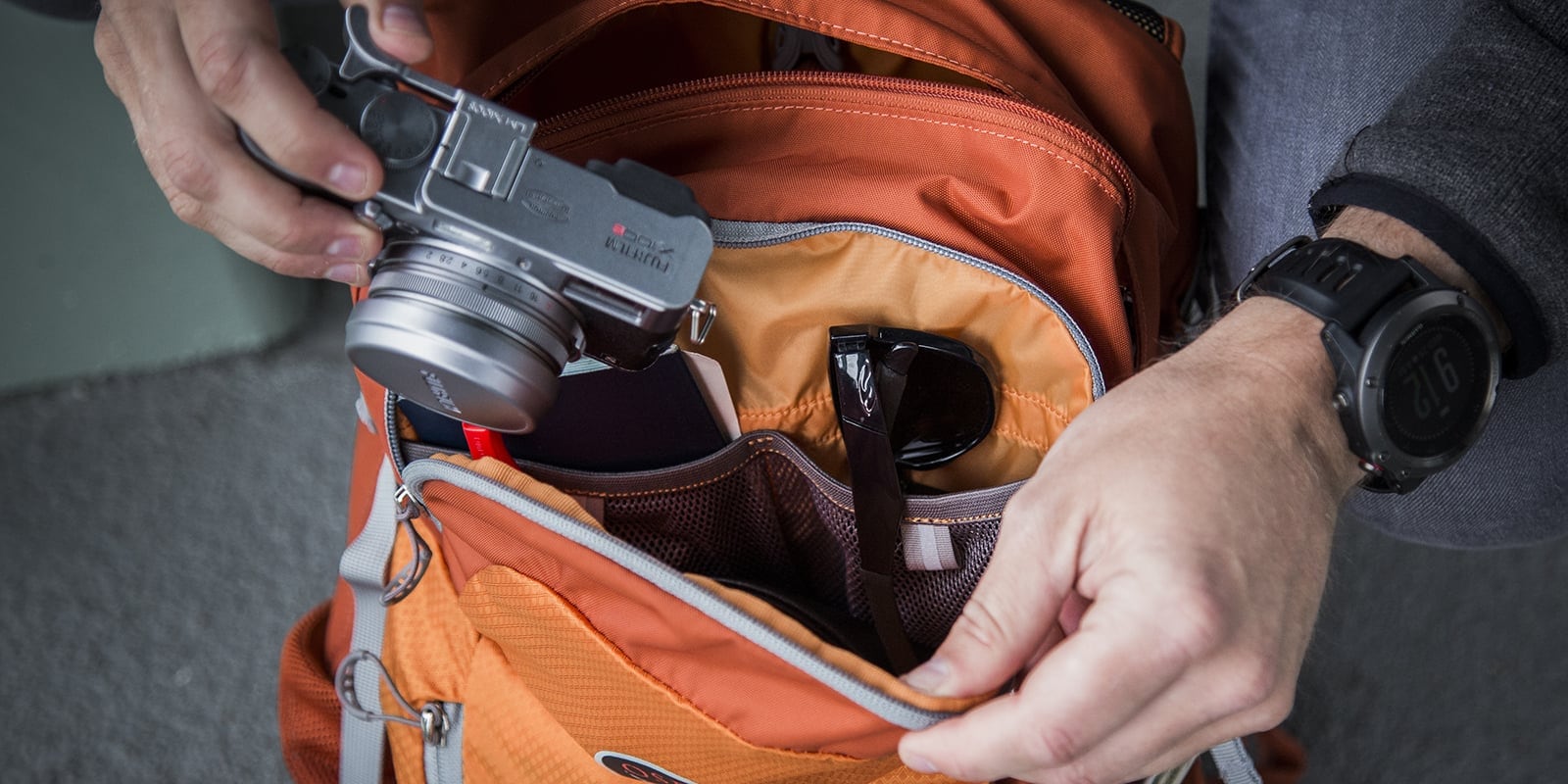 Close up of someone's hands packing a camera into an orange backpack