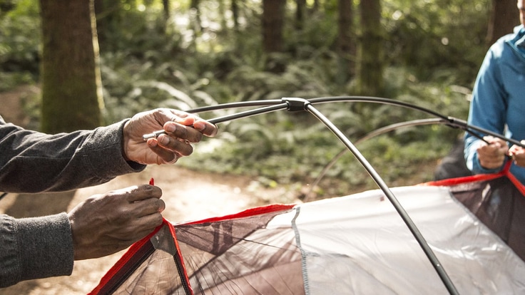 two campers connect tent poles to tent