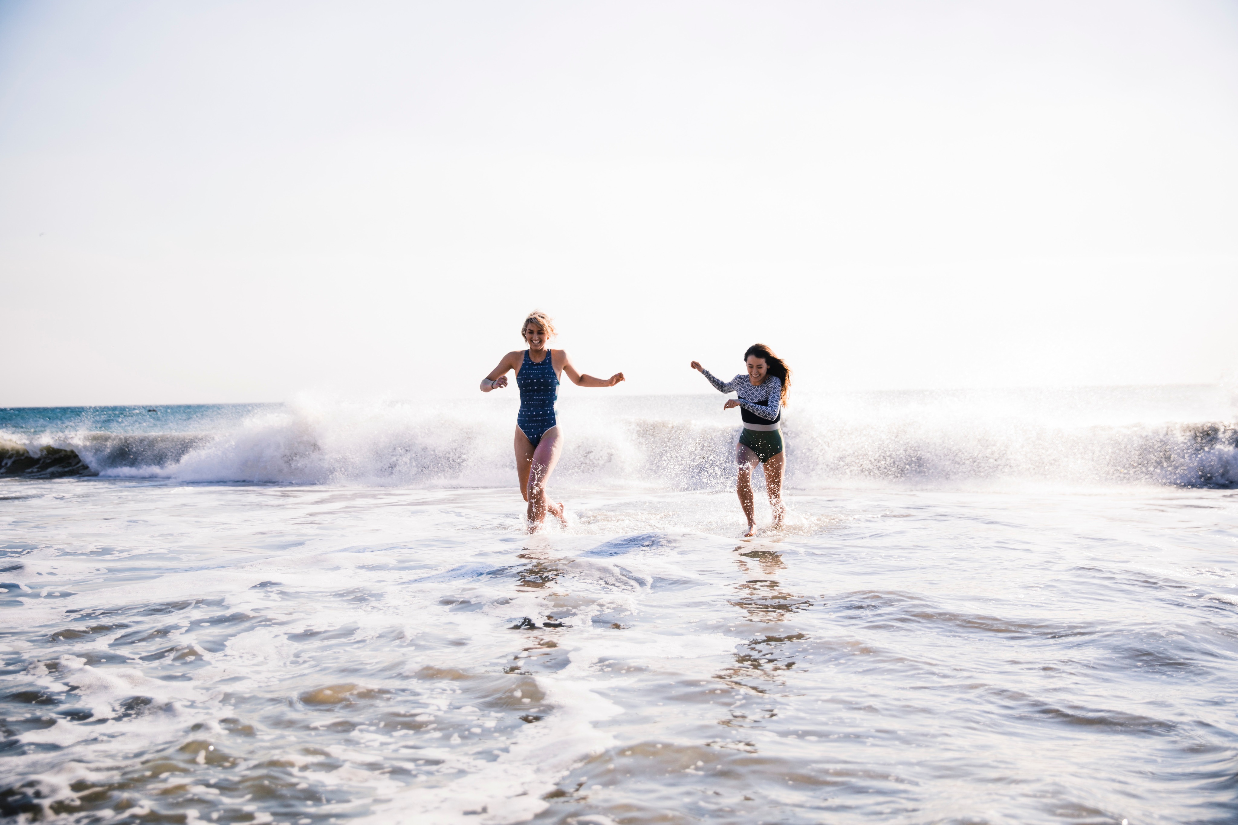 Two women wearing swimsuits are running out of the ocean water smiling