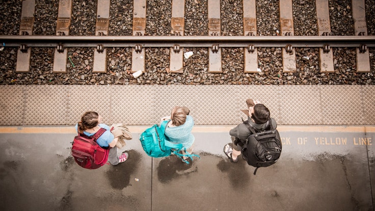 Three travelers with backpacks on a train platform