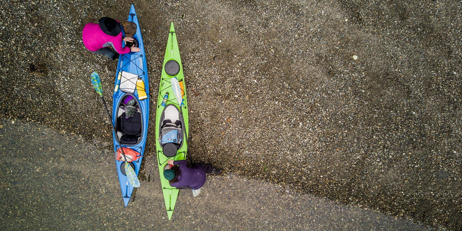 An aerial view of two kayakers on a beach preparing to launch their kayaks