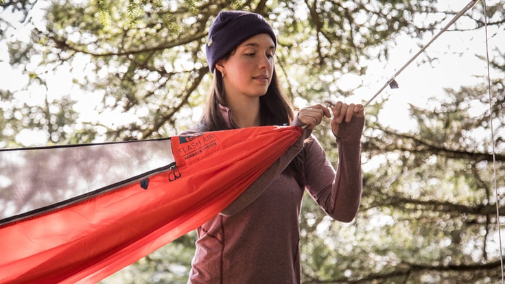 A woman hanging her hammock from a tree