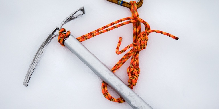 an ice axe, rope, and carabiner on the snow