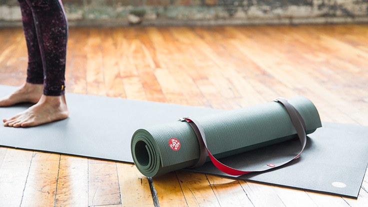 Person standing on a yoga mat with a rolled up mat sitting on top