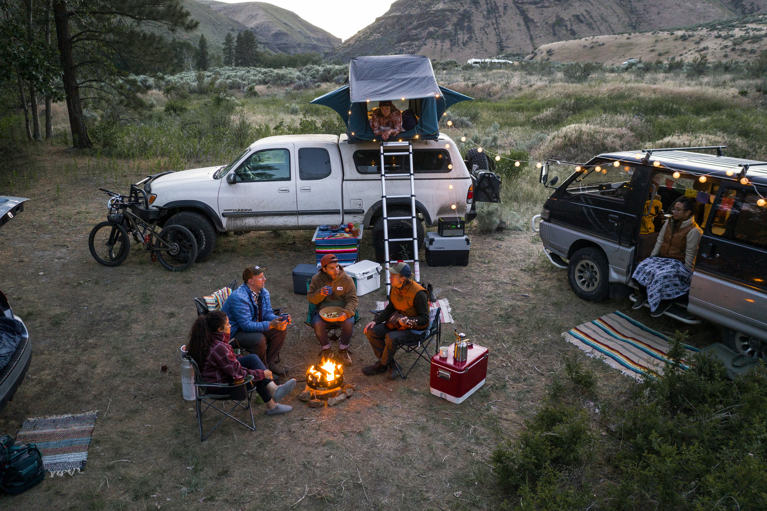 A group of campers sit in a circle, surrounded by their vehicles; one has a rooftop tent attached to it.