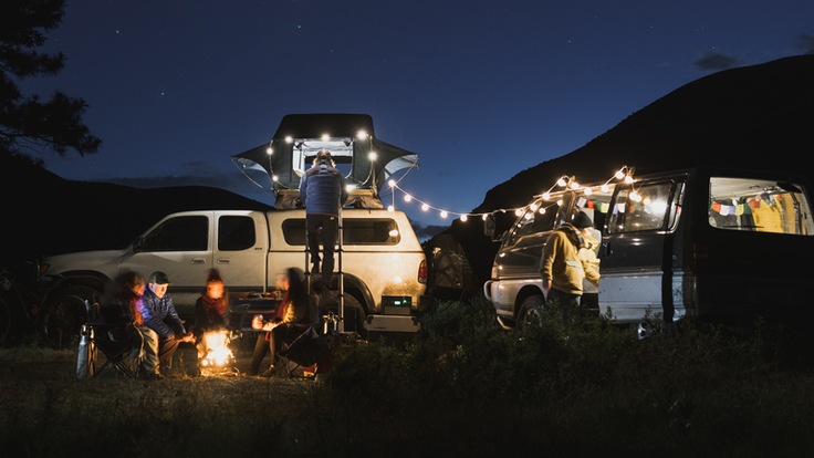 A rooftop tent set up in a campsite at night