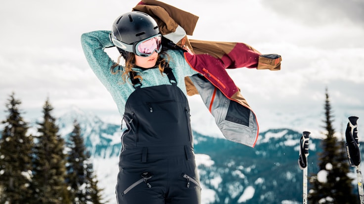 A skier puts on a jacket over her bibs