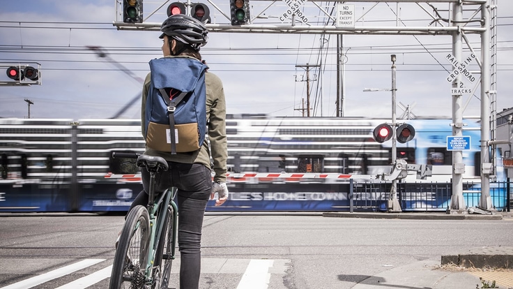 A commuter cyclist waits at a controlled crossing for a passenger train to pass