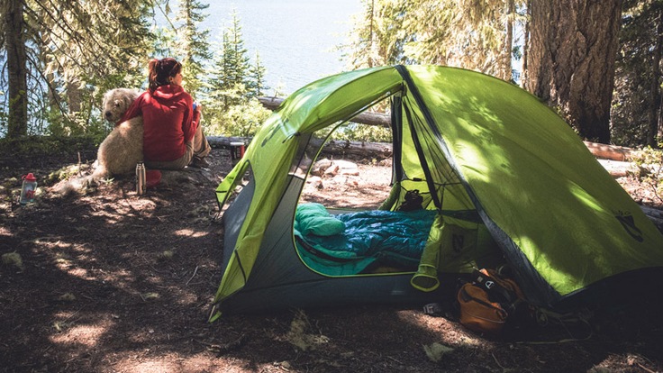 a backpacker and her dog sitting outside their backpacking tent and campsite