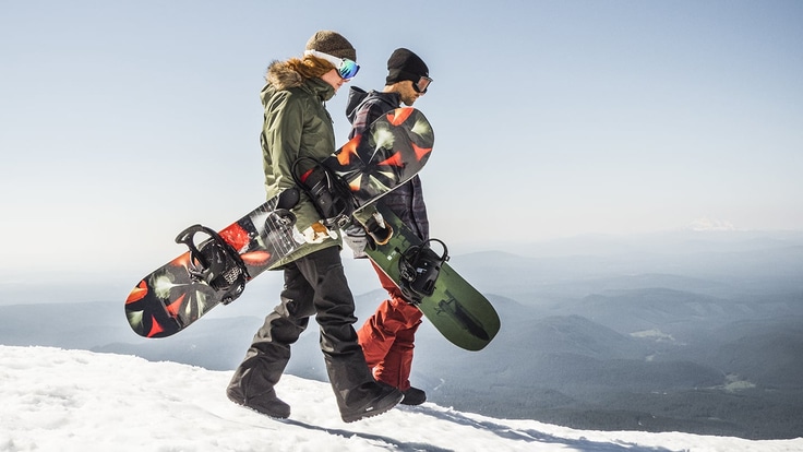 Two snowboarders carrying their boards