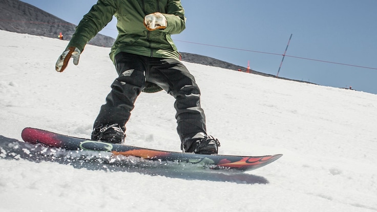 Close up of a snowboarders legs and board while going down a run