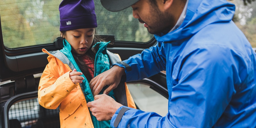 Man zips up a young girl's coat.