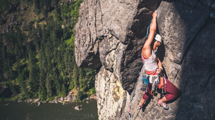 A woman rock climbing above a river