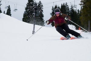 Femal skier urns down the mountain in black ski pants and a burgundy and brown jacket