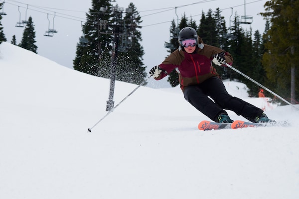 Femal skier urns down the mountain in black ski pants and a burgundy and brown jacket