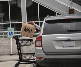 An R E I customer reaches out their card window to pick up their items from a cart.
