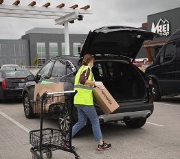 An R E I employee places a Curbside Pickup order inside a customer's vehicle.
