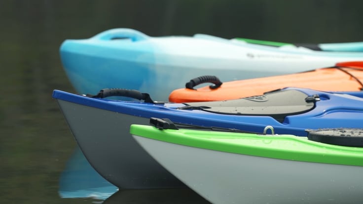 Close-up photo of the bows of four kayaks on the water.
