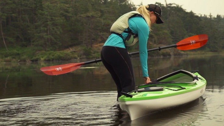 A woman stands in the water with her kayak preparing to launch it
