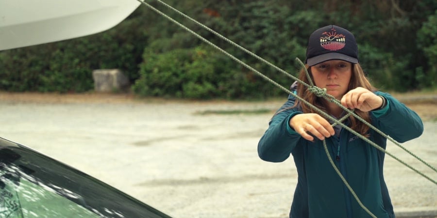 a kayaker tying down the bow of a kayak to the front of their vehicle