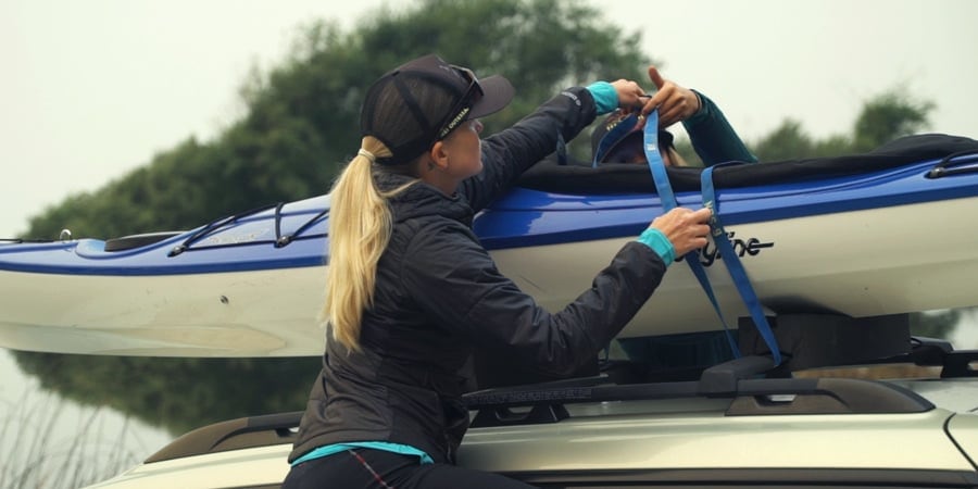 applying tie down straps to a kayak placed on top of a vehicle roof rack