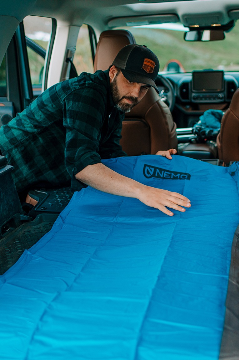 A person lays out their blue NEMO Quasar 3D Insulated Air Sleeping Pad in the back of their vehicle.