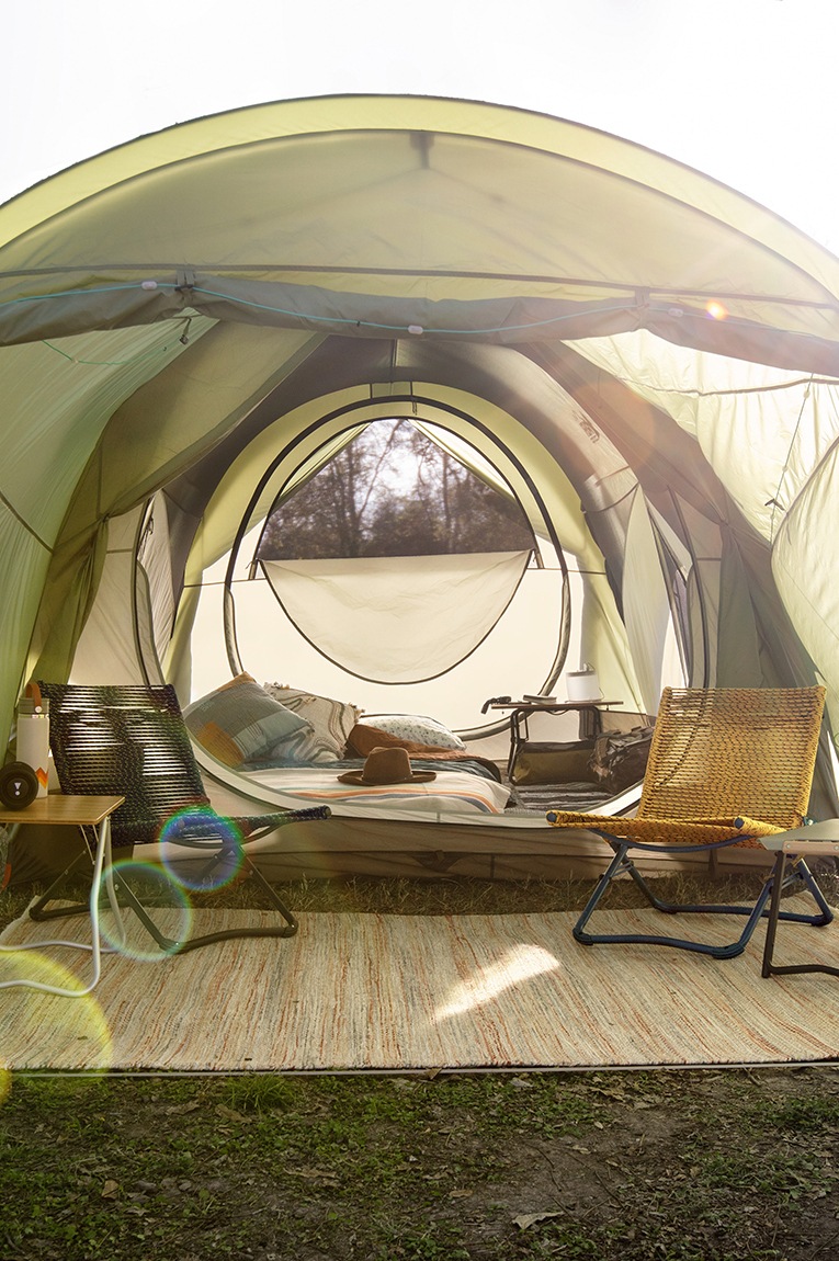 The Wonderland 6 Tent with its entryway open to an outdoor mat and camp chairs, and behind it, a cot and side table inside the tent.
