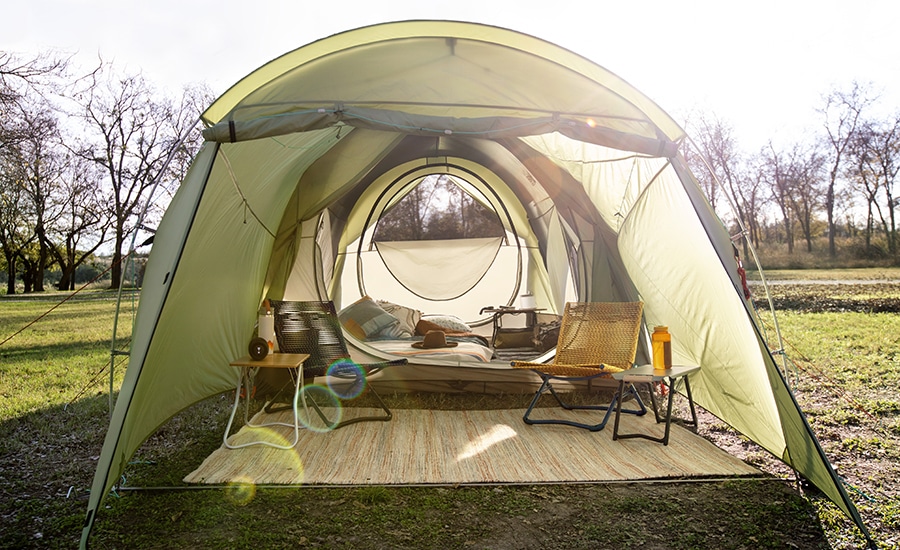 The Wonderland 6 Tent with its entryway open to an outdoor mat and camp chairs, and behind it, a cot and side table inside the tent.