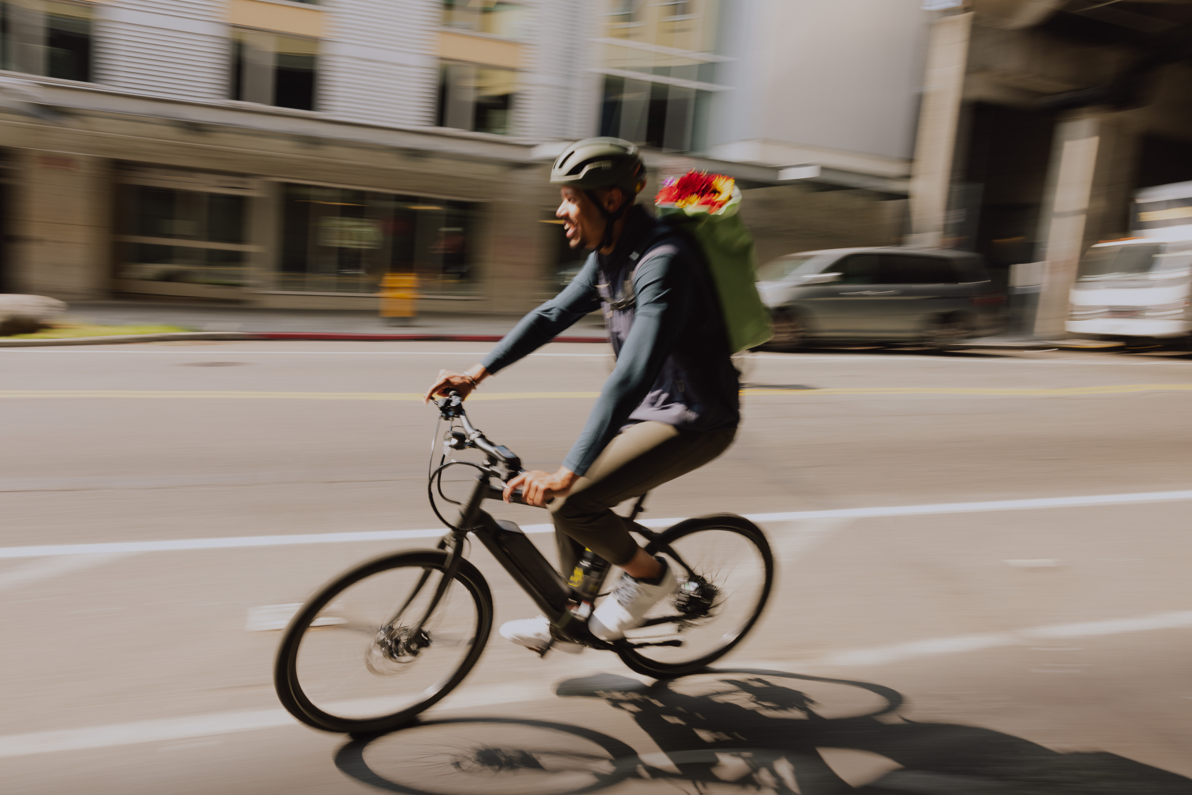 A person carrying flowers in a backpack pedals an electric bike through town