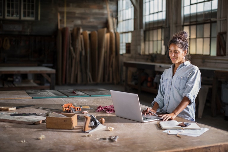 Woman standing at a table working on a laptop with tools around her