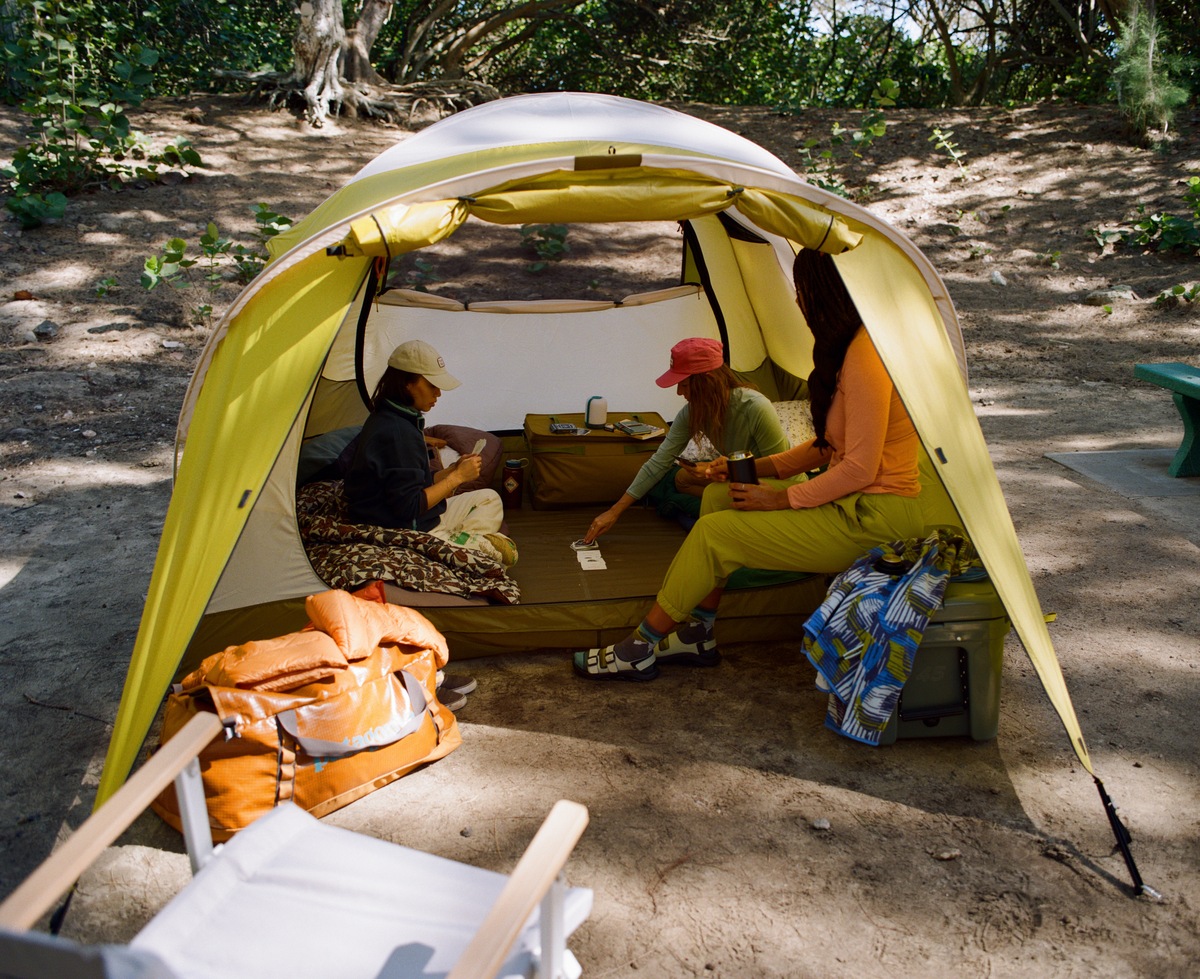 Three campers sit in a tent playing cards.