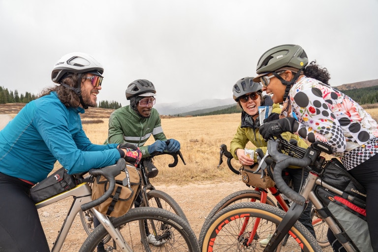 Four cyclists gather together in a circle. They each wear different cycling jerseys and jackets.