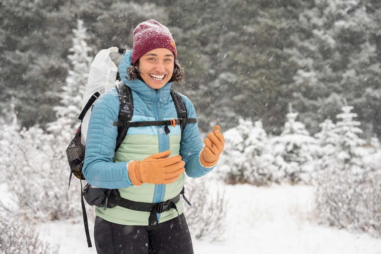 A person wears gloves and a colorful insulated jacket while hiking in snow.