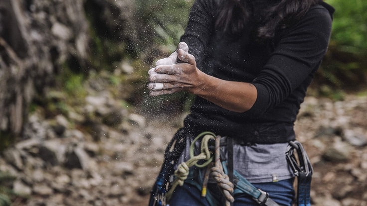 Close up of a rock climber's torso clapping her hands together after covering them in chalk.