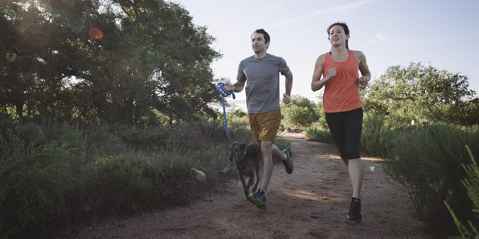 a couple trail running with their dog on a leash