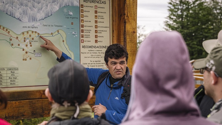 Guide using a large map on a wooden sign to show his travel group where they are headed